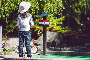 Little girl wearing a sun hat on a miniature golf course.